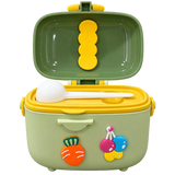 A green and yellow plastic lunch box with a hinged lid, shown open with a white ladle inside. The front has colorful cartoon food decorations, including a carrot and three hanging fruit charms.