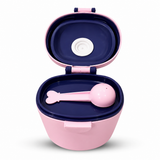 A pink and navy blue baby feeding container with an open lid, featuring a pink spoon with a bone-shaped handle and a white nipple shield inside.