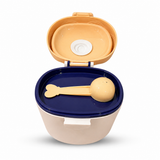 A baby feeding container with an open lid, featuring a beige exterior, a navy blue inner tray, and a matching beige spoon resting inside.
